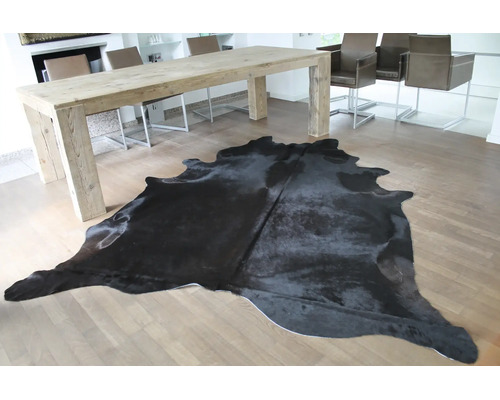 Ein schwarzes Kuhfell auf hellem Parkett in einem hellen, modernen Esszimmer mit großem Holztisch.