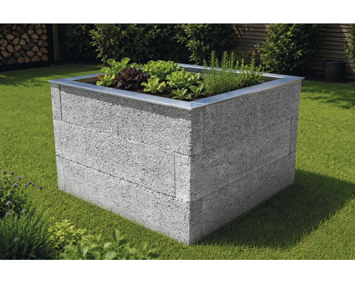Quadratisches Hochbeet aus grauen Mauersteinen mit Metallkante, bepflanzt mit Salat und Kräutern auf einer Rasenfläche.