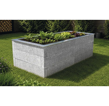 Hochbeet aus grauen Steinen mit einer Metalleinfassung auf einer Rasenfläche im Garten, bepflanzt mit verschiedenen Salaten.