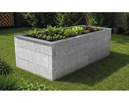 Hochbeet aus grauen Steinen mit einer Metalleinfassung auf einer Rasenfläche im Garten, bepflanzt mit verschiedenen Salaten.