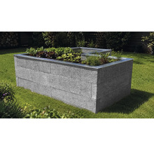 L-förmiges Hochbeet aus grauen Mauersteinen mit Metallkante, bepflanzt mit Gemüse und Kräutern auf einer Rasenfläche im Garten.