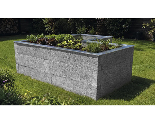 L-förmiges Hochbeet aus grauen Mauersteinen mit Metallkante, bepflanzt mit Gemüse und Kräutern auf einer Rasenfläche im Garten.