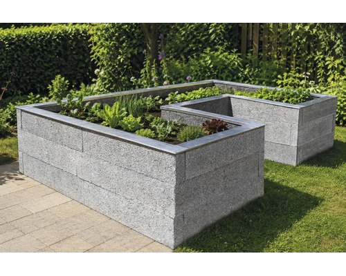 L-förmiges Hochbeet aus hellgrauen Steinblöcken mit Metalleinfassung, bepflanzt mit Gemüse und Kräutern in einem Garten auf einer Rasenfläche.