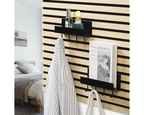 Schwarze Metallregale mit Haken an einer Wand aus Holzlamellen in einem modern eingerichteten Schlafzimmer mit Buch, Flaschen und Kleidung.