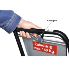 Hand am Handgriff einer Transportkarre mit Bremshebel und einem Schild für die maximale Zuladung von 140 Kilogramm.