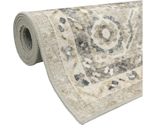 Aufgerollter Teppich im Vintage-Stil mit Medaillon-Muster und geketteltem Rand in Beige und Grau.