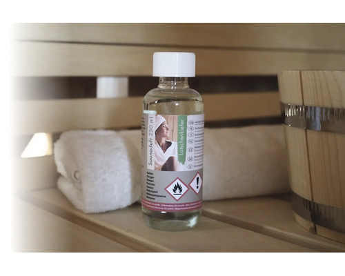 Saunaduft Latschenkiefer 250 Milliliter Flasche auf einer hölzernen Saunabank neben einem Handtuch und einem Saunakübel.