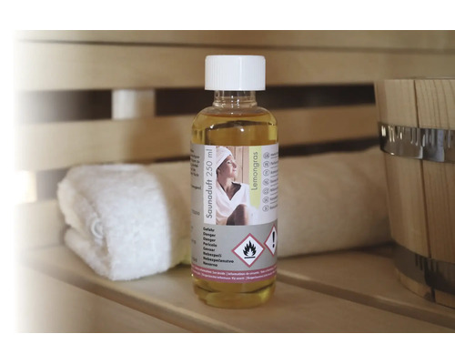 Saunaduft Lemongras 250 Milliliter in einer Flasche auf einer Holzbank in einer Sauna neben einem Handtuch und einem Saunakübel.