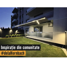 Beleuchtete Gelenkarmmarkise mit integrierten LED Streifen über einem Balkon mit Glasgeländer und einer gepflegten Rasenfläche bei Nacht.