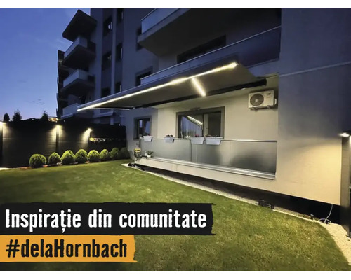 Beleuchtete Gelenkarmmarkise mit integrierten LED Streifen über einem Balkon mit Glasgeländer und einer gepflegten Rasenfläche bei Nacht.