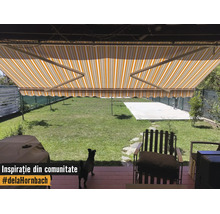 Gelb-weiß gestreifte Gelenkarmmarkise über einer Terrasse mit Blick auf einen grünen Garten und Gartenmöbeln.