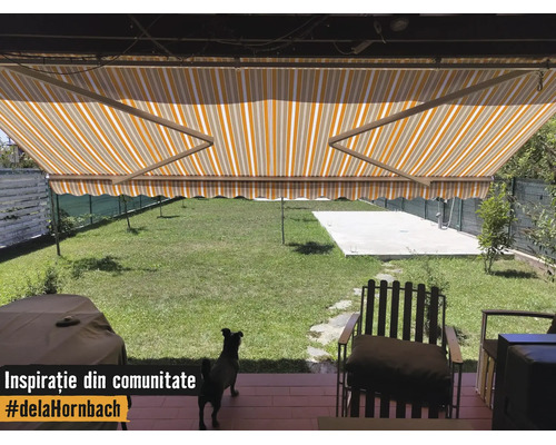 Gelb-weiß gestreifte Gelenkarmmarkise über einer Terrasse mit Blick auf einen grünen Garten und Gartenmöbeln.