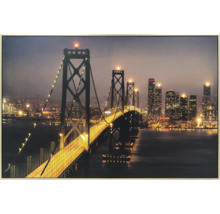 Gerahmtes Wandbild mit beleuchteter Hängebrücke und nächtlicher Stadtsilhouette.