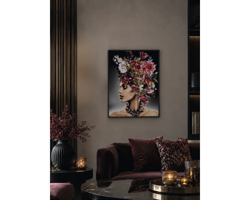 Wohnzimmer mit beleuchtetem Wandbild einer Frau mit Blumenkopfschmuck, dunklem Samtsofa und stimmungsvoller Beleuchtung durch Kerzen.