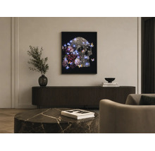 Ein gerahmtes Wandbild mit einem Totenkopf, Blumen, Schmetterlingen und blauen LED-Lichtern über einem dunklen Sideboard in einem modernen Wohnzimmer.