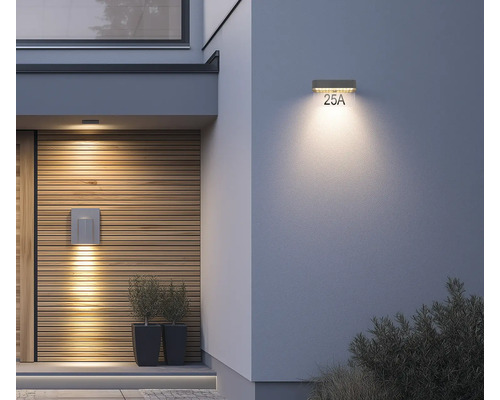 Moderne Außenwandleuchte und Solar-Hausnummernleuchte LED an einem Hauseingang mit Holzfassade und verputzter Wand.