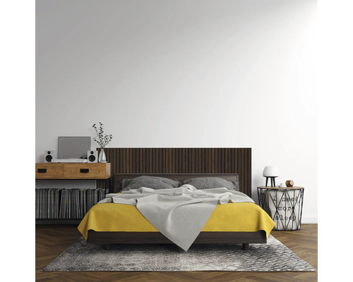 Modernes Schlafzimmer mit Doppelbett, dunkelbraunem Kopfteil in Holzlatten-Optik, gelber Bettwäsche, Fischgrätparkett und grauem Teppich.