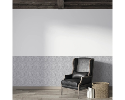 Helle Wandgestaltung mit Vliestapete in Steinoptik unten und weißer Wand darüber. Schwarzer Leder-Ohrensessel auf Parkett unter Holzbalkendecke.