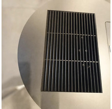 Nahaufnahme eines rechteckigen schwarzen Lüftungsgitters aus Metall, das in eine kreisförmige Edelstahloberfläche eingelassen ist.
