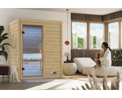 Moderne Innensauna aus hellem Holz mit Glastür in einem hellen, wohnlichen Wellnessbereich mit Liege und Frau im Bademantel.