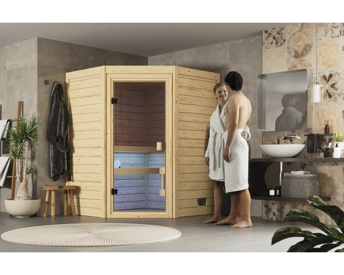 Eine Ecksauna aus Holz steht in einem modern gestalteten Badezimmer, in dem ein Paar in Bademänteln vor der Saunatür steht.