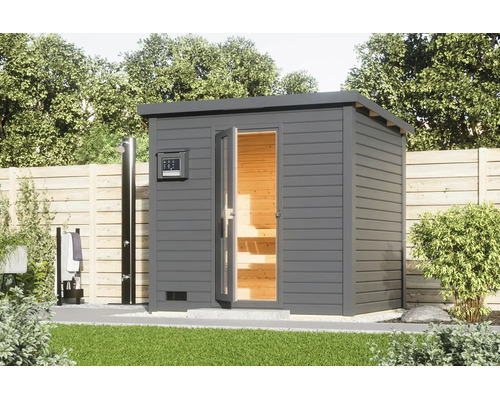 Moderne Garten-Sauna mit Pultdach und Ganzglastür, aufgestellt im Garten neben einer Gartendusche vor einem Holzzaun.