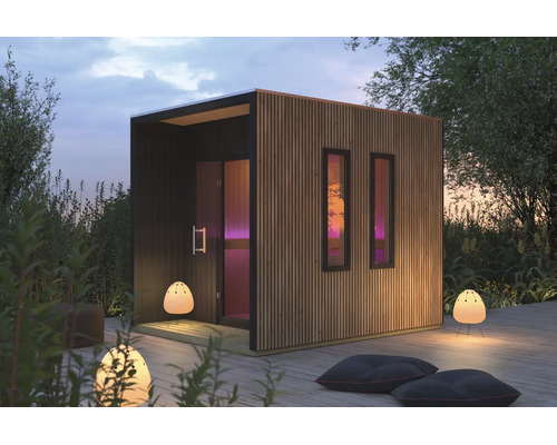 Moderne Gartensauna aus Holz mit Flachdach und Lamellenverkleidung auf einer Holzterrasse im Garten bei Dämmerung.