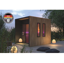 Moderne Karibu Gartensauna mit Holzlamellen Fassade und zwei Fenstern, aufgestellt auf einer Holzterrasse mit Außenbeleuchtung und Sitzkissen.