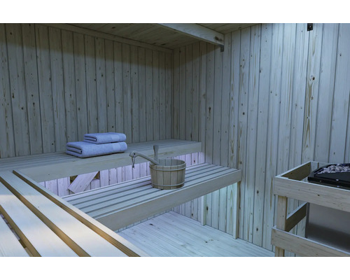 Innenansicht einer modernen Holzsauna mit abgestuften Saunabänken, Saunakübel und Handtüchern sowie einem Saunaofen.