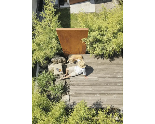 Person mit Hund auf einer Holzterrasse aus Dielen, umgeben von Bambuspflanzen und einer Sichtschutzwand aus Cortenstahl.