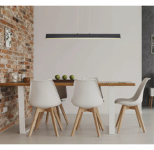 Moderne schwarze lineare LED-Pendelleuchte über einem Esstisch aus Holz mit weißen Stühlen in einem Raum mit einer Ziegelwand.