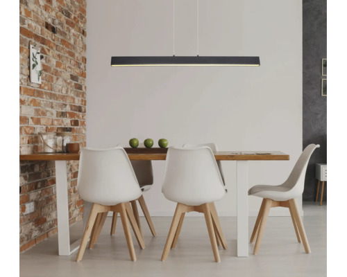 Moderne schwarze lineare LED-Pendelleuchte über einem Esstisch aus Holz mit weißen Stühlen in einem Raum mit einer Ziegelwand.