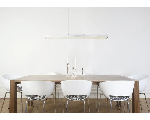 Moderne, lineare Pendelleuchte über einem Holzesstisch mit weißen Designerstühlen in einem hellen, freundlichen Esszimmer.