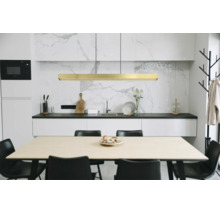 Moderne Küche mit goldener LED-Pendelleuchte über einem Holztisch, schwarzen Stühlen, weißen Schränken und Marmorrückwand.