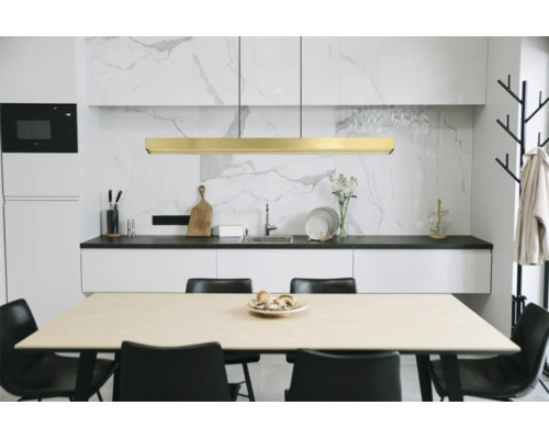 Moderne Küche mit goldener LED-Pendelleuchte über einem Holztisch, schwarzen Stühlen, weißen Schränken und Marmorrückwand.