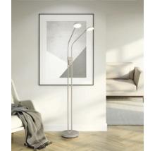 Moderne, minimalistische Stehleuchte mit zwei flexiblen LED-Lichtköpfen in einem hellen Wohnzimmer mit Parkettboden und abstrakter Wandkunst.