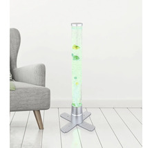 Beleuchtete Wassersäule mit dekorativen Fischen, silberfarbenem Standfuß und Luftblasen neben einem grauen Sessel auf hellem Holzboden.