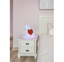 Leuchtende, irisierende geometrische LED-Deko-Figur Bär mit rotem Herz auf einem weißen Nachttisch im Schlafzimmer.