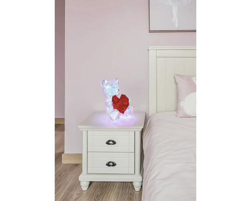 Leuchtende, irisierende geometrische LED-Deko-Figur Bär mit rotem Herz auf einem weißen Nachttisch im Schlafzimmer.