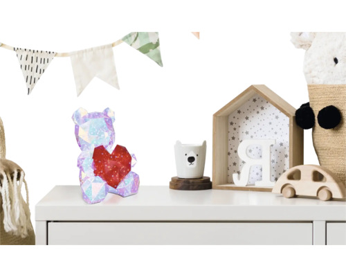 Kindliches Kinderzimmer mit Dekoration wie einem glitzernden Bären mit Herz, Girlande und Holzspielzeug auf einer weißen Kommode.
