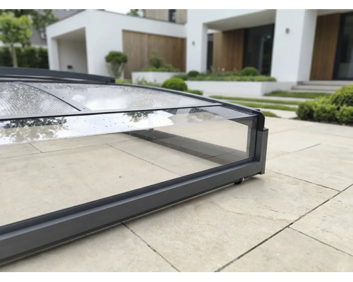 Nahaufnahme einer Poolüberdachung mit dunkelgrauem Aluminiumrahmen und transparenten Polycarbonatplatten auf einer Steinterrasse.