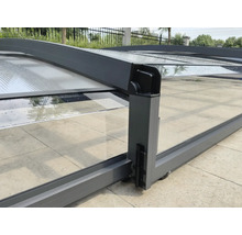 Schiebbare Poolüberdachung aus Aluminium mit transparenten Paneelen, Rollen und Verriegelung auf einer gepflasterten Terrasse.