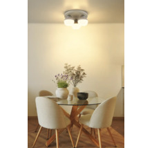 Moderne Deckenleuchte mit drei weißen Glaskugeln über einem runden Glastisch mit Holzbeinen und gepolsterten Stühlen.