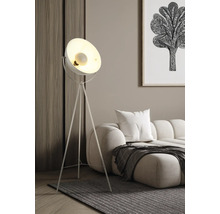 Moderne Dreibein-Stehleuchte mit Metallschirm in einem hellen Wohnzimmer neben einem Sofa und einem Teppich.