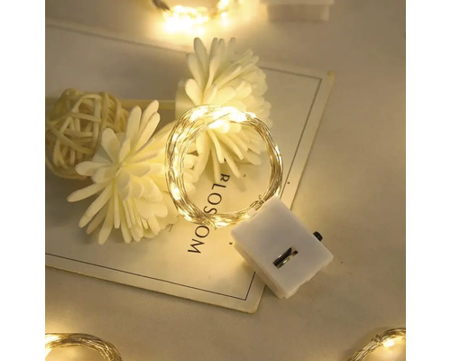 LED-Draht-Lichterkette mit Batteriegehäuse, dekorativ arrangiert mit Kunstblumen auf einer Karte.