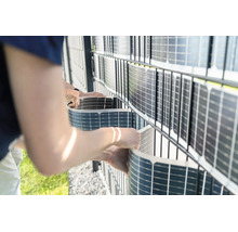 Person montiert flexible Solarmodule als Sichtschutz an einem Doppelstabmattenzaun im Garten.