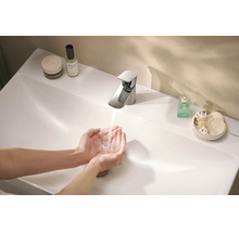Hände waschen an einer modernen Hansgrohe Waschtischarmatur über einem weißen Waschbecken mit Kosmetikartikeln im Badezimmer