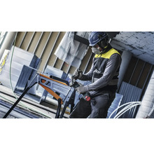 Handwerker mit Schutzausrüstung schneidet ein Metallrohr mit einem Akku Winkelschleifer auf einem klappbaren Arbeitstisch.