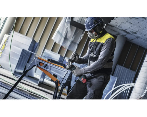 Handwerker mit Schutzausrüstung schneidet ein Metallrohr mit einem Akku Winkelschleifer auf einem klappbaren Arbeitstisch.