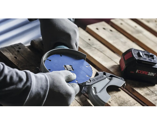 Person mit Handschuhen beim Wechseln der Trennscheibe eines Bosch Akku Winkelschleifers auf einer Holzpalette